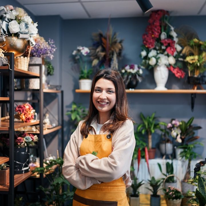 Femme souriante en tablier, entourée de plantes et fleurs dans une boutique. Femme souriante en tablier, entourée de plantes et fleurs dans une boutique.