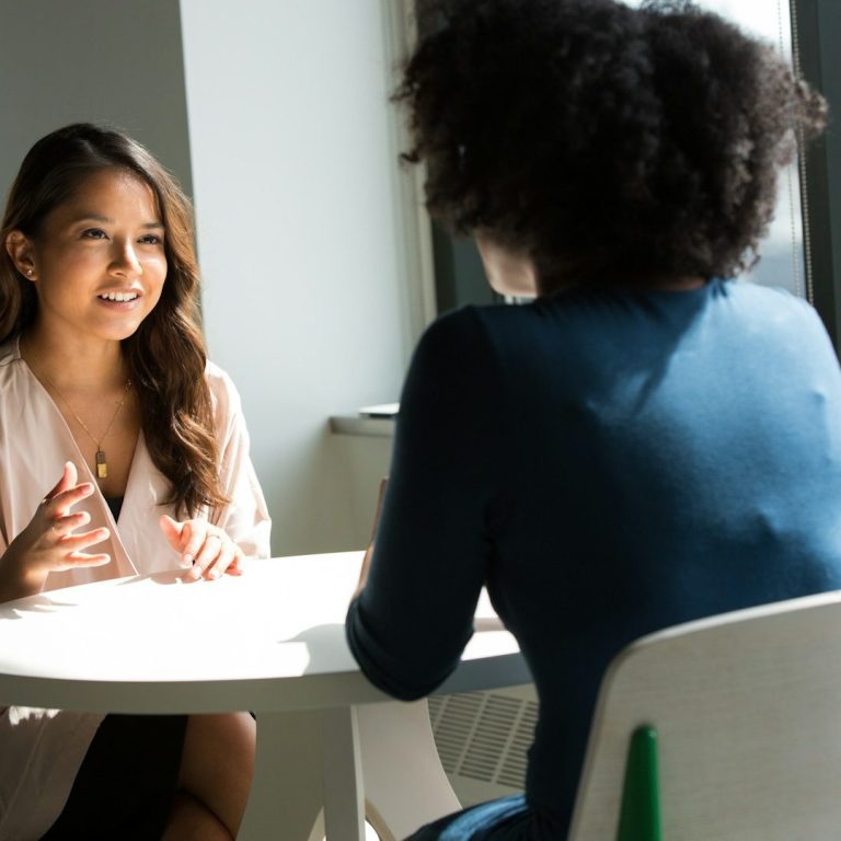 Deux femmes discutent autour d'une table, l'une souriante et expressive. Deux femmes discutent autour d'une table, l'une souriante et expressive.