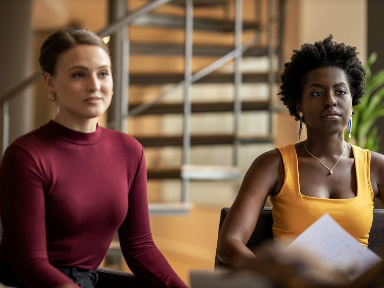 Deux femmes assises, l'une en pull rouge et l'autre en débardeur jaune, avec une plante en arrière-plan. Deux femmes assises, l'une en pull rouge et l'autre en débardeur jaune, avec une plante en arrière-plan.