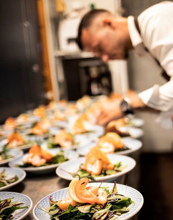Un chef prépare des assiettes garnies de saumon et de plantes à la cuisine. Un chef prépare des assiettes garnies de saumon et de plantes à la cuisine.